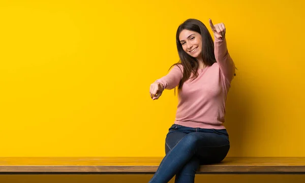 Mujer Joven Sentada Mesa Señala Con Dedo Mientras Sonríe —  Fotos de Stock