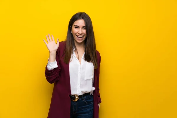 黄色の壁が幸せな表情で手で敬礼の若い女性 — ストック写真