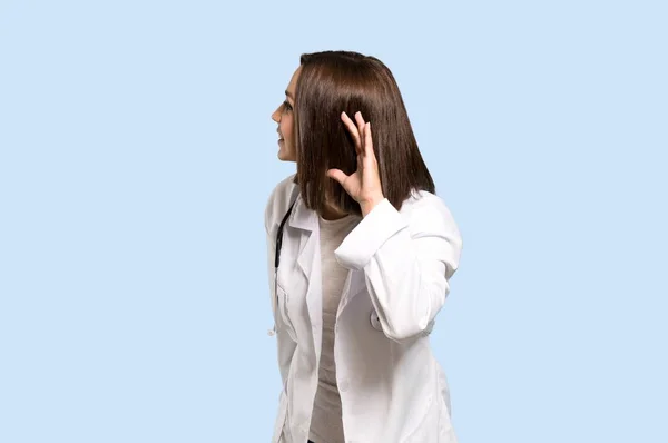 若い医者分離の青い背景に耳に手を置くことによって何かを聞く女性 — ストック写真