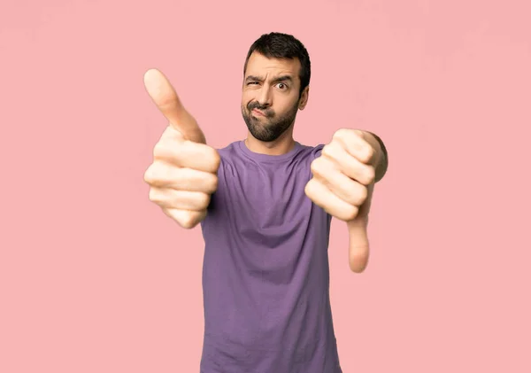Handsome man making good-bad sign. Undecided between yes or not on isolated pink background