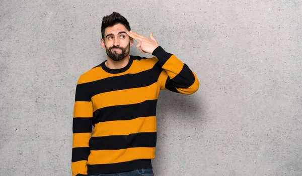 Handsome man with striped sweater with problems making suicide gesture over textured wall