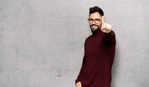 Handsome man with glasses showing and lifting a finger over textured wall