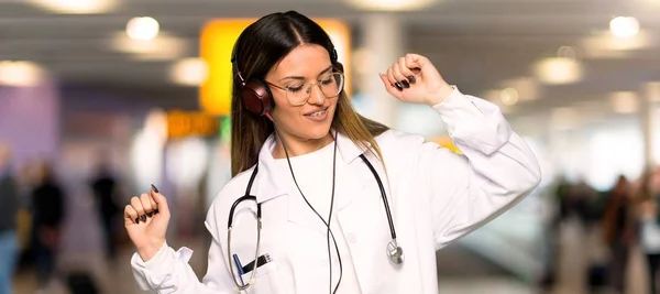 Young doctor woman listening to music with headphones and dancing in a hospital