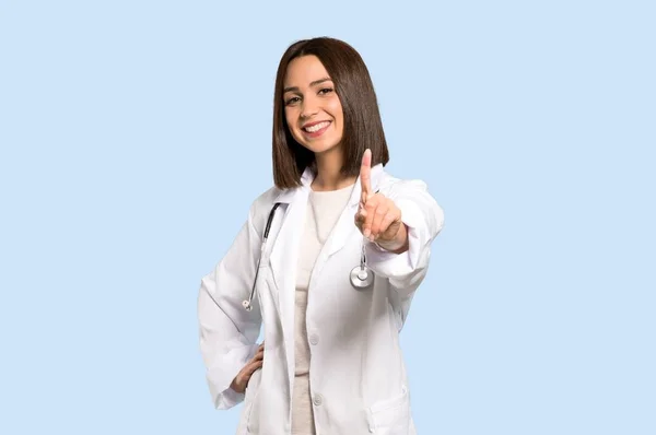 年轻的医生妇女展示和举一个手指在被隔绝的蓝色背景 — 图库照片