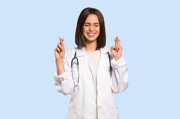Joven Doctora Con Dedos Cruzando Deseando Mejor Sobre Fondo Azul — Foto de Stock