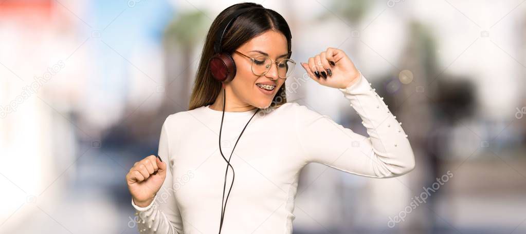 Pretty woman with glasses listening to music with headphones and dancing at outdoors