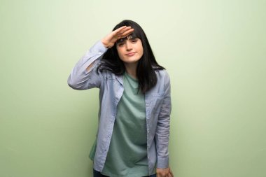 Yeşil duvara uzak bir şey bakmak için el ile görünümlü genç kadın