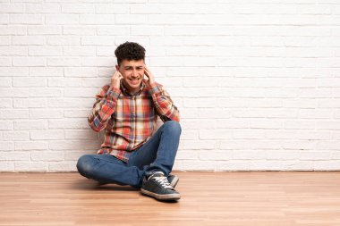 Yerde oturan genç adam sinirli ve kulakları kapsayan