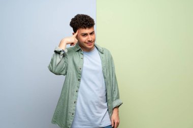 Mavi ve yeşil arka plan üzerinde genç adam delilik jest kafasına parmak koyarak yapma