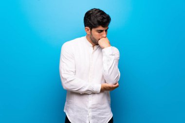 İzole mavi duvar üzerinde genç adam şüpheleri var