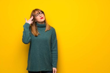 Sarı duvarın üstünde gözlüklü bir kadın intihar jesti yapıyor.