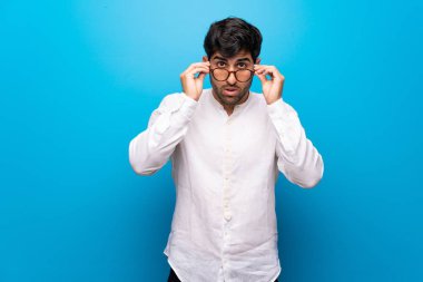 Gözlük ile izole mavi duvar üzerinde genç adam ve sürpriz