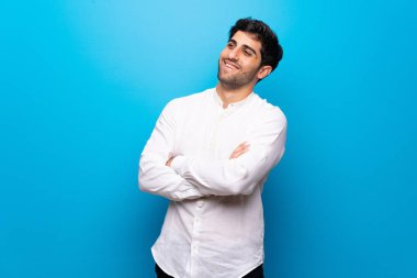 Gülümseyen iken izole mavi duvar üzerinde genç adam silah geçti tutmak