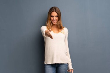 İyi bir anlaşma kapanış için eller sallayarak gri arka plan üzerinde sarışın kadın