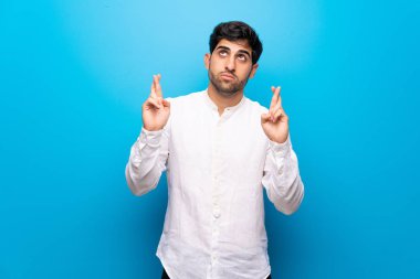 En iyi dilek ve geçiş parmak ile izole mavi duvarın üzerinden genç adam