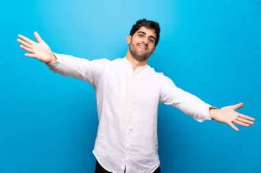 İzole mavi duvar üzerinde genç adam sunma ve el ile gelmek için davet