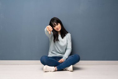 Yerde oturan kadın, negatif ifade ile başparmak aşağı gösteren