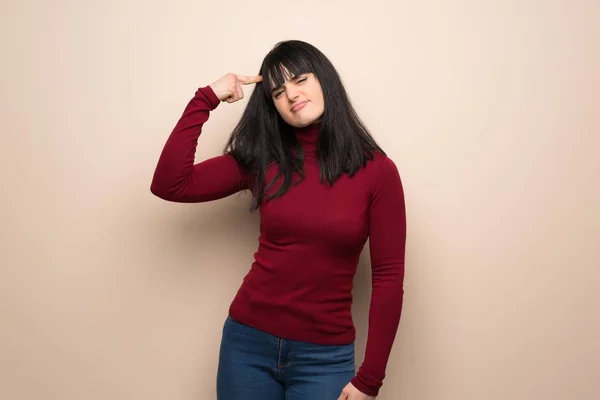 Young woman with red turtleneck making the gesture of madness putting finger on the head