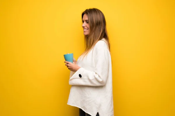 熱い一杯のコーヒーを保持している黄色の壁を越えて金髪女性 — ストック写真
