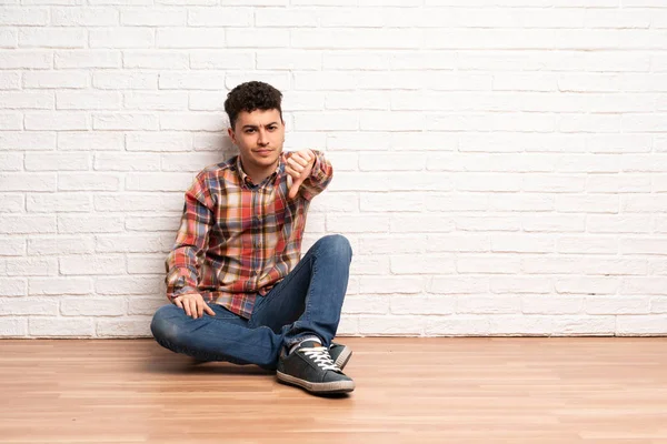 Mladý Muž Sedí Podlaze Zobrazeno Palec Negativní Výraz — Stock fotografie
