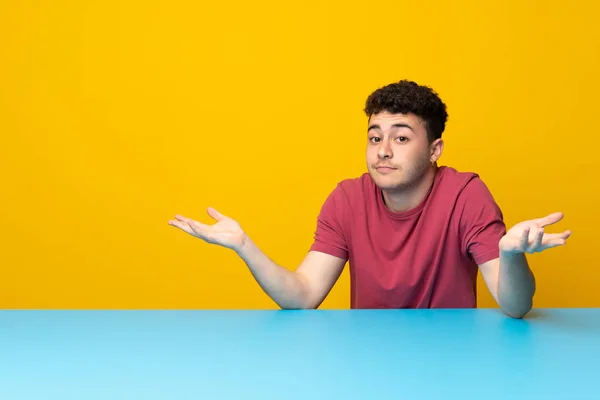 Jovem Com Parede Colorida Mesa Com Dúvidas Levantar Mãos — Fotografia de Stock