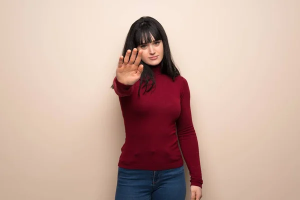 Young woman with red turtleneck making stop gesture denying a situation that thinks wrong