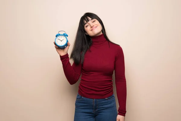 Young woman with red turtleneck holding vintage alarm clock
