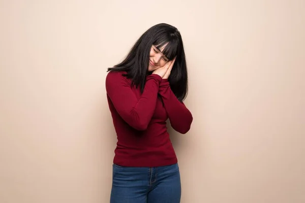 Young woman with red turtleneck making sleep gesture in dorable expression