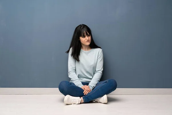 Woman sitting on the floor with confuse face expression while bites lip