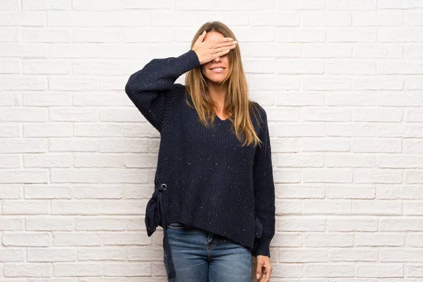 Blonde woman over brick wall covering eyes by hands. Surprised to see what is ahead