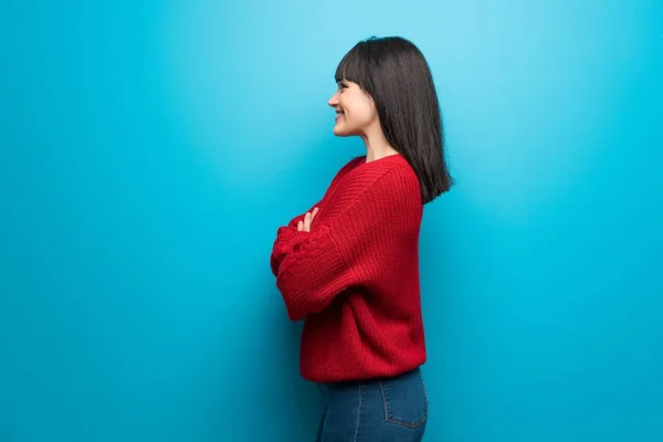 Woman with red sweater over blue wall in lateral position