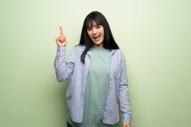 Yeşil duvar üzerinde genç kadın bir parmak yukarı kaldırarak çözüm gerçekleştirirken niyetle