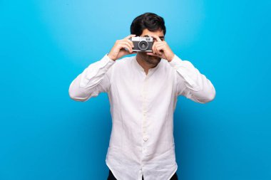 Genç adam bir kamera tutarak izole mavi duvarın üzerinden
