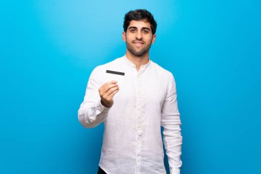 Bir kredi kartı tutan izole mavi duvar üzerinde genç adam