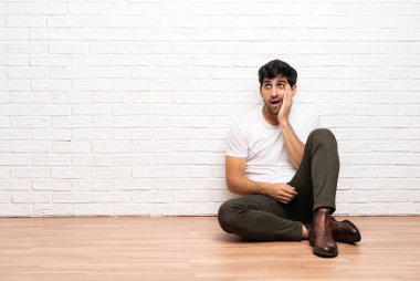 Sürpriz ve şok yüz ifadesi ile yerde oturan genç adam