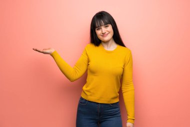 Pembe duvar üzerinde sarı kazak ile kadın bir reklam eklemek için avuç hayali boşaltmak tutan