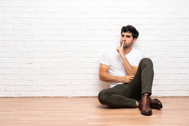 Genç adam yerde oturan sessiz jest ağzına parmak koyarak bir işareti gösteren