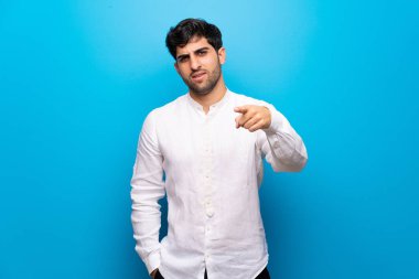 İzole mavi duvar üzerinde genç adam sinirli ve ön işaret