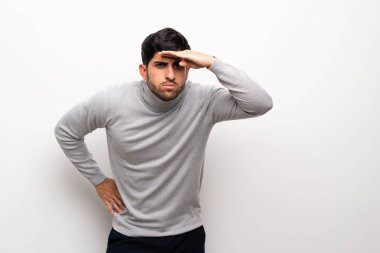 İzole beyaz duvar üzerinde genç adam uzak bir şey bakmak için el ile bakıyor