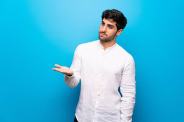 Genç adam üzerinde izole mavi duvar bir fikir sunma sırasında gülümseyen bakarak