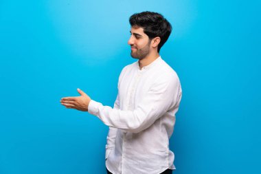 İyi bir anlaşma sonra izole mavi duvar el sallama üzerinde genç adam