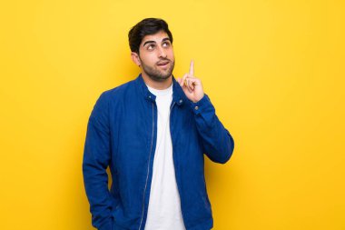 Sarı duvara mavi ceket ile adam parmak işaret bir fikir düşünme