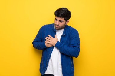 Kalp bir ağrı sahip sarı duvar üzerinde mavi ceket ile adam