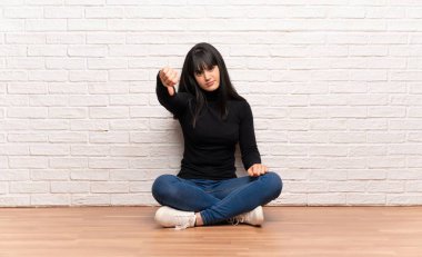 Yerde oturan kadın, negatif ifade ile başparmak aşağı gösteren