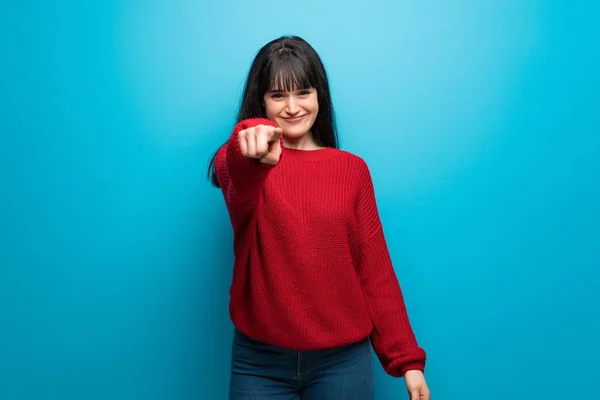 Woman with red sweater over blue wall points finger at you with a confident expression