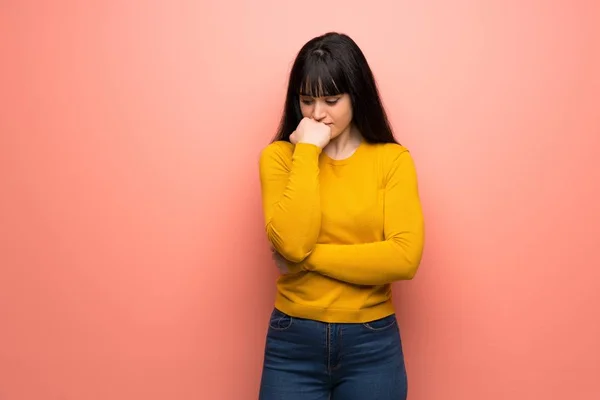 Woman with yellow sweater over pink wall having doubts