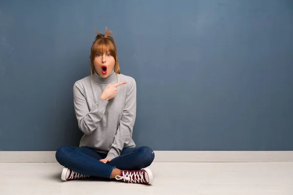 Rothaarige Frau Sitzt Überrascht Auf Dem Boden Und Zeigt Auf — Stockfoto