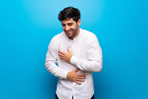 Young man over isolated blue wall smiling a lot while putting hands on chest