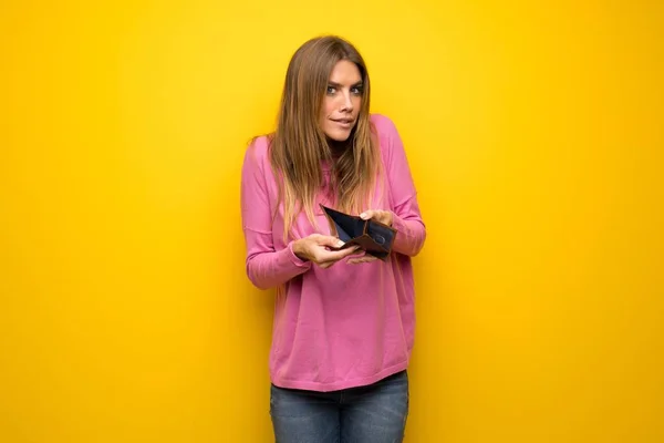 財布を保持している黄色の壁にピンクのセーターの女性 — ストック写真