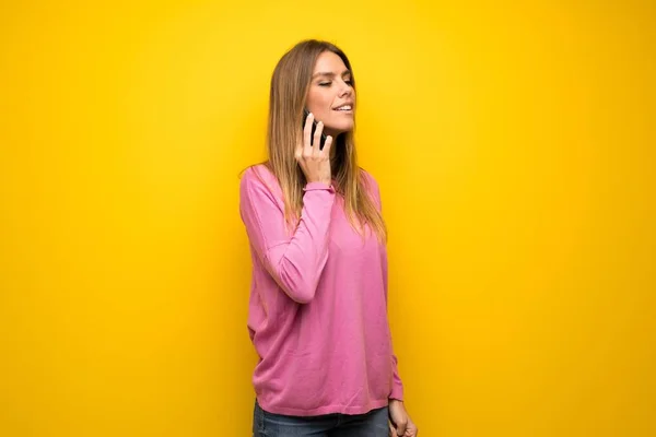 黄色い壁の上にピンクのセーターを持った女性携帯電話との会話を維持する — ストック写真